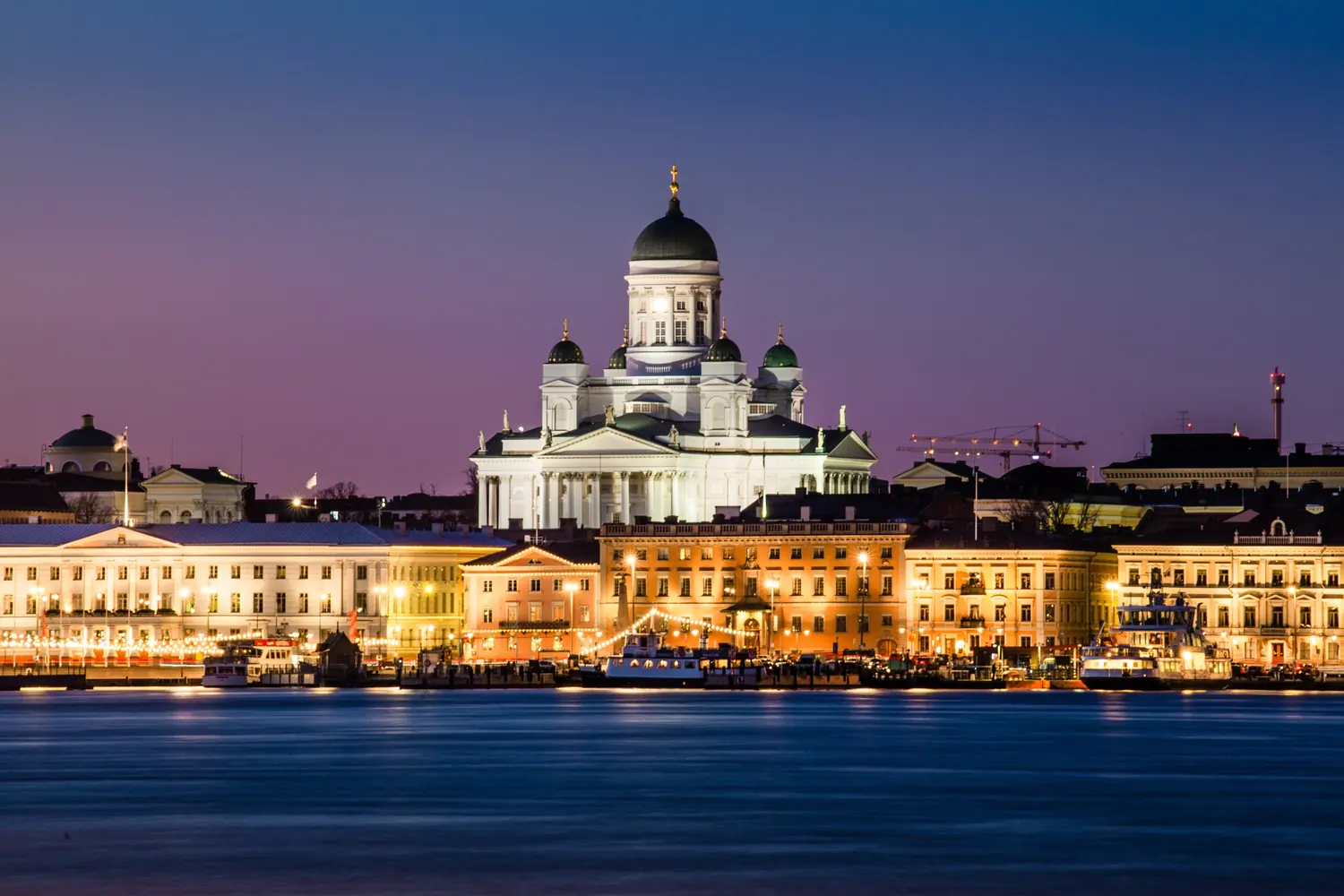 Helsinki Cathedral and the harbour front lit up at dusk, seen across the water
