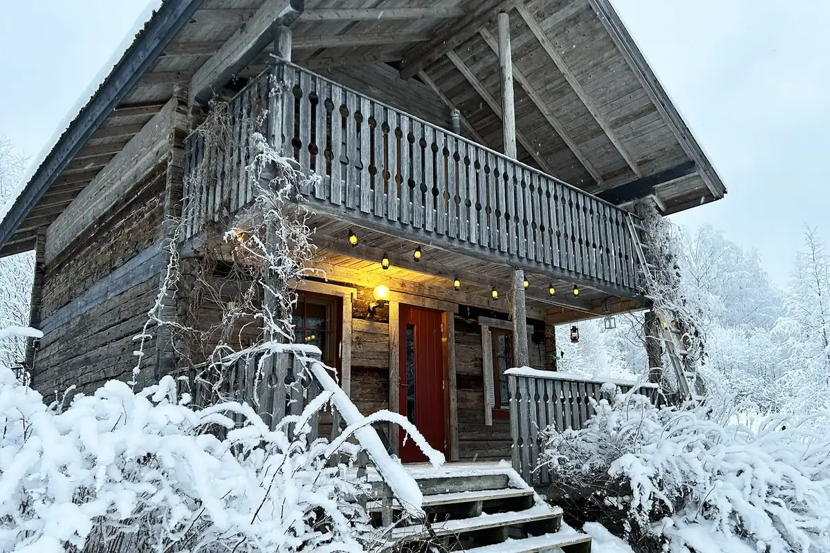 Snow-covered log cabin with a lantern-lit porch near Tahko